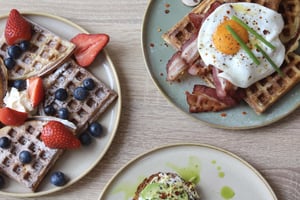 Ein süßes und herzhaftes Frühstück mit Waffeln, garniert mit Beeren, und Avocado-Toast mit Speck und Ei